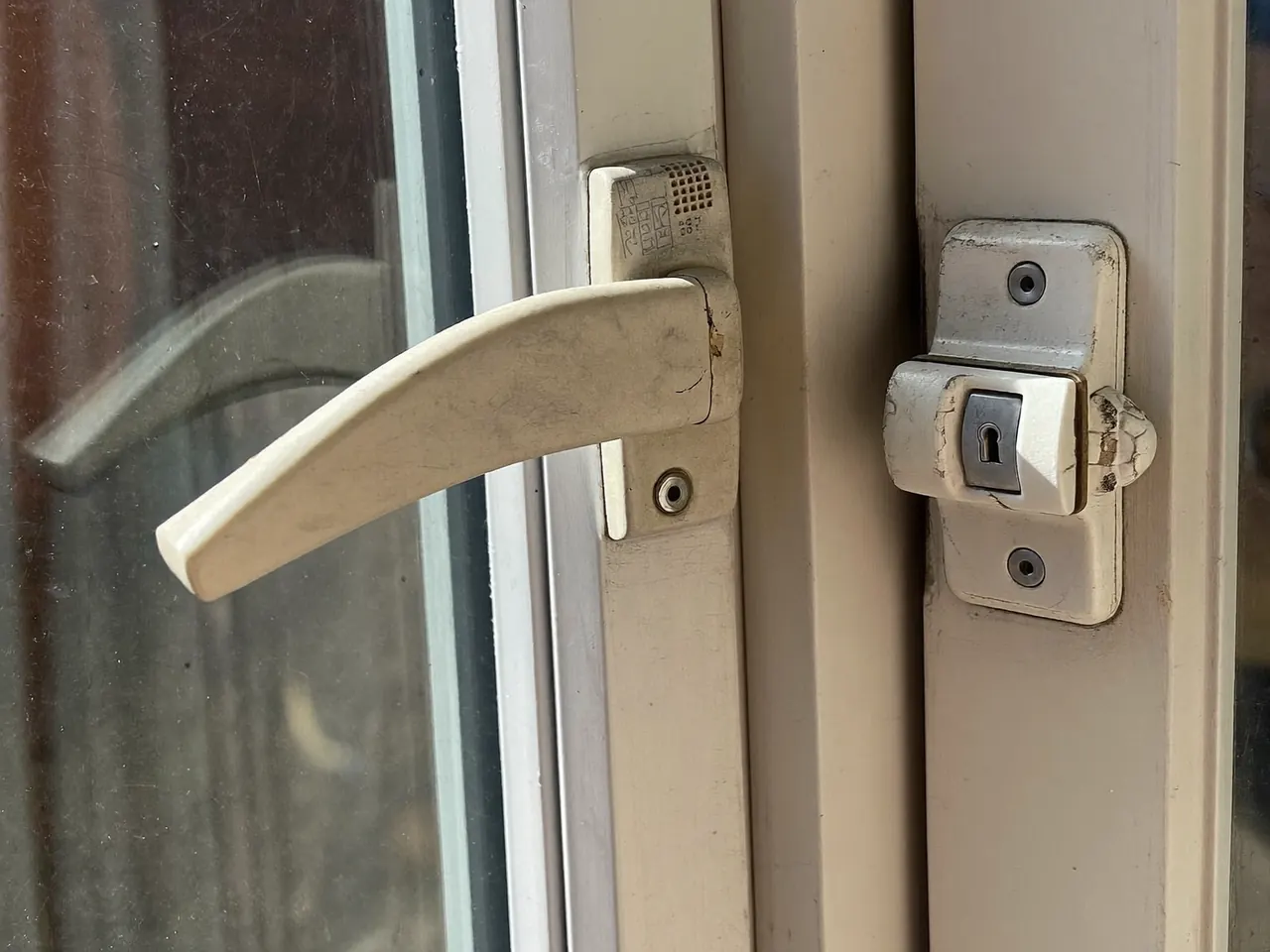 Close-up of a worn window handle and lock on a uPVC frame